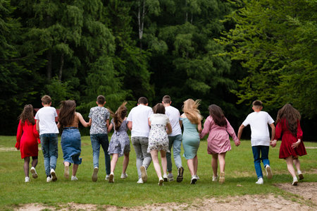 A group of teenagers joyfully run through a grassy park, hands linked, showcasing friendship and carefree fun against a backdrop of lush greenery.の写真素材