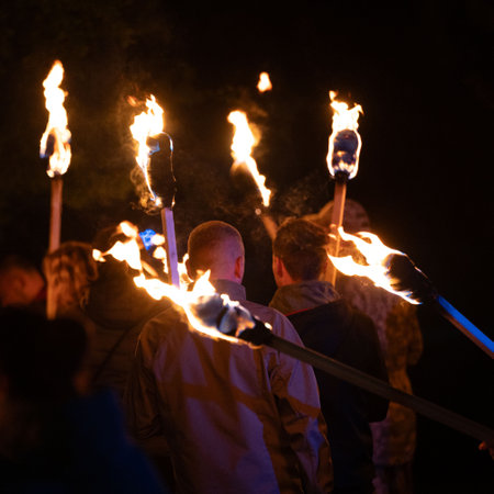 Several individuals walk in the dark, each holding a burning torch aloft. The flames illuminate their backs, creating a striking visual contrast against the night sky.の写真素材