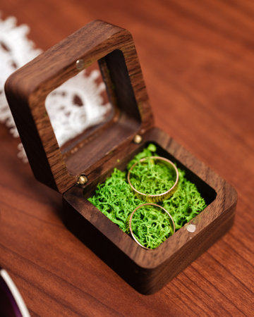 Close-up of two golden rings resting on vibrant green moss within an elegant wooden box. The box is made of dark wood and has a glass top.の写真素材
