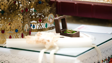 Close-up of wedding rings nestled in a small wooden box. Ornate gold crowns are visible in the background, suggesting a ceremony or religious context.の写真素材