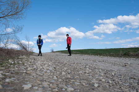 A boy and a man stroll along a gravel road. The sky is clear, with fluffy clouds. The scene suggests a rural or countryside setting. The atmosphere is calm and serene.の写真素材