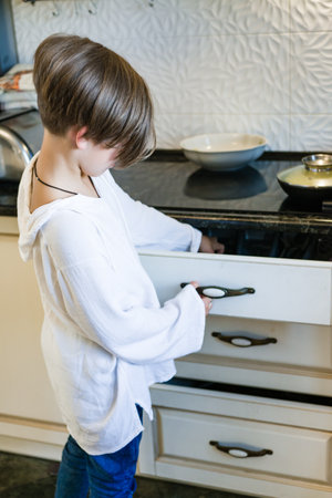 A young person observes an adult carefully pour pancake batter into a frying pan on a modern electric stove.の写真素材