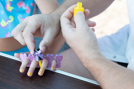 A child receives a manicure, a grown-up carefully applies yellow nail polish to their tiny fingernails.の写真素材