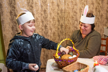 A boy and woman, both wearing handmade bunny ear headbands, gather decorated Easter eggs and bread...