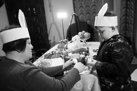 Two children, adorned with DIY bunny ear headbands, are carefully arranging eggs in a basket. A...