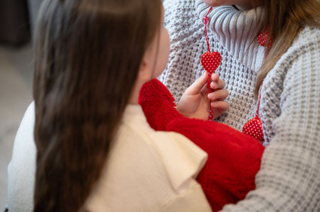 Close-up of a young girl and adult woman, possibly mother and daughter, sharing a tender moment. The woman shows the girl a necklace with red heart-shaped pendants.の写真素材