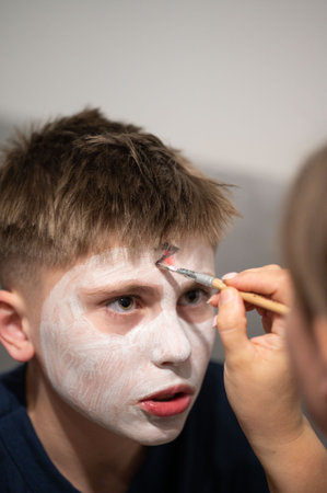 Close-up view of a child getting their face painted white by an adult. The setting appears to be a casual indoor environment, perhaps a home.の写真素材