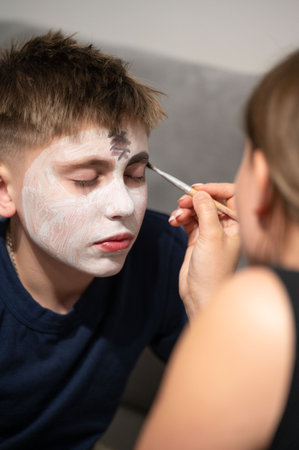 Close-up view of a person having their face painted, focusing on the detail of the application and the model's expression. The setting appears to be indoors.の写真素材