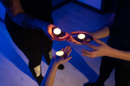 Close-up view of three people's hands carefully cradling small, burning candles in a dimly lit room. The scene evokes a sense of ritual or contemplation.の写真素材