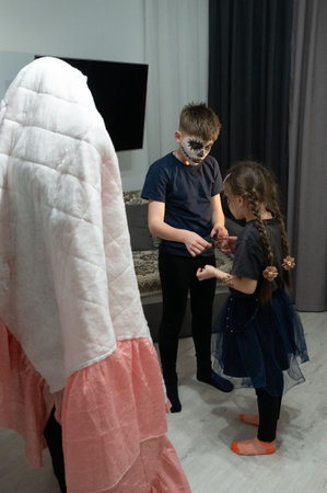 Three children are preparing for a costume party. One child is hidden under a sheet, another has...