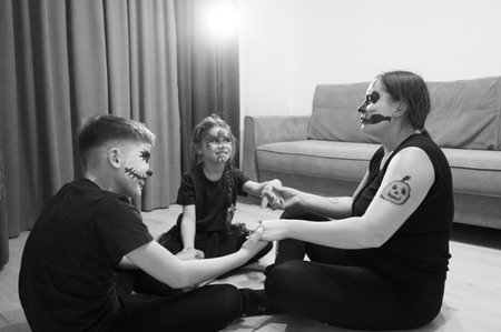 Three individuals, a woman and two young children, sit on the floor in a living room setting, all...