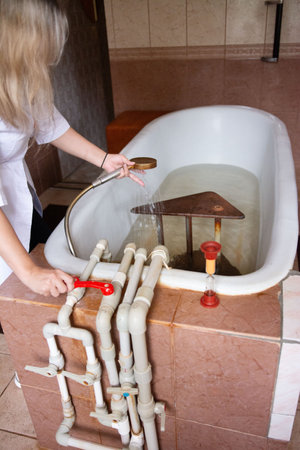 A therapist is preparing a bath, equipped with intricate pipework and a metal contraption within the water, for a specialized therapeutic treatment.の写真素材