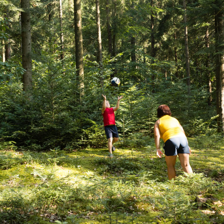 A boy and a woman enjoy a game of catch in a lush forest. Sunlight filters through the trees, illuminating the mossy ground.の写真素材