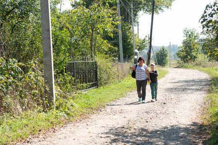 A woman and a child are walking hand in hand down a dirt path on a sunny day. The path is surrounded by trees and greenery, creating a peaceful and scenic atmosphere.の写真素材