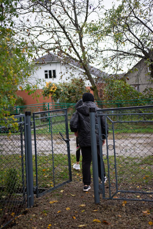 A person in a black padded jacket walks through an open metal fence gate, with another person partially visible behind them.の写真素材