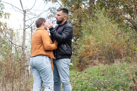 In a tranquil forest setting, a couple shares a loving interaction, embracing the warmth of their bond as colorful autumn leaves create a picturesque backdrop.の写真素材