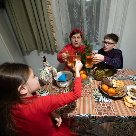 A grandmother, boy, and girl raise glasses of a warm beverage around a table laden with fruit and...