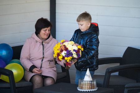 A joyful interaction unfolds as a young boy offers a vibrant bouquet to a smiling woman, highlighting love and connection in a cheerful atmosphere with balloons.の写真素材