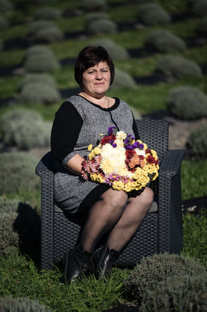 A woman sits peacefully among lush lavender fields, cradling a colorful bouquet of fresh flowers, showcasing the beauty of nature and vibrant artistry in her surroundings.の写真素材