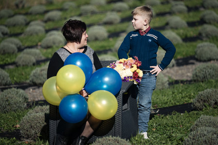 A woman and a boy share a delightful moment in a lavender field, surrounded by colorful balloons and a bouquet of flowers under the warm autumn sun.の写真素材