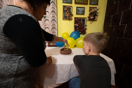 A joyful gathering unfolds as a woman prepares to light a candle on a cake, watched closely by a young boy amidst cheerful decorations and balloons.の写真素材
