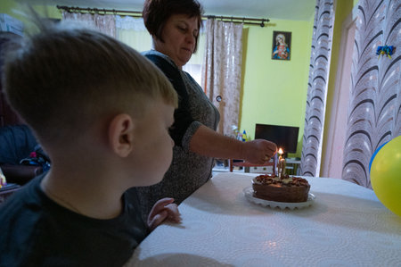 A woman lights a candle on a chocolate cake while a young boy watches with excitement in a warmly decorated living room, creating a memorable birthday moment.の写真素材