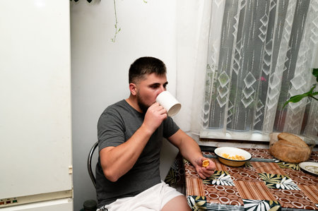 Sipping coffee while savoring a light breakfast, the individual embraces the calm of a morning at home, surrounded by simple comforts and soft light.の写真素材