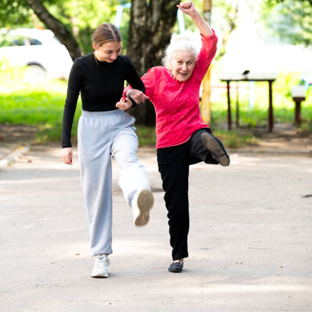 Smiling grandmother and granddaughter doing sports together in the park. Old and young women do a warm-up. They walk along the sidewalk, bouncing.の写真素材
