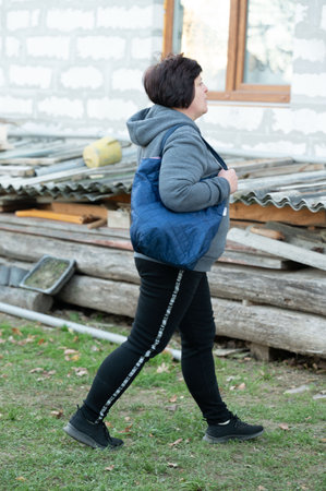 In the warm late afternoon, a woman casually strolls through the countryside in a hoodie and leggings, carrying a blue bag and enjoying the peaceful surroundings.の写真素材
