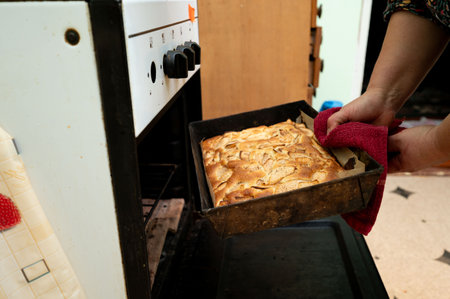 A hand gently pulls a tray of golden apple dessert from the oven, wrapping it in a cozy towel, as warm scents fill the inviting kitchen on a peaceful afternoon.の写真素材