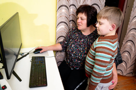 Joyful interaction unfolds as a young child observes intently while an adult engages with a computer, both immersed in moments of discovery and shared amusement.の写真素材