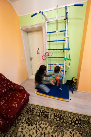 Bright colors fill a cheerful room where a young child engages with a climbing frame, fostering curiosity and physical activity with guidance from a loving adult.の写真素材