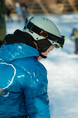 A young skier dons a bright blue jacket and helmet, focused on the snowy terrain, with fellow skiers enjoying the slopes in the background under a clear winter sky.の写真素材