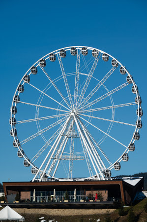 Visitors admire the impressive structure of a giant observation wheel against a vibrant blue sky, enjoying a sunny afternoon at the amusement park with friends and family.の写真素材