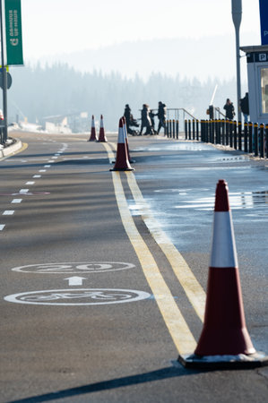 Morning light casts a serene glow on a quiet avenue lined with traffic cones, as people stroll and cyclists navigate carefully past the peaceful scenery.の写真素材