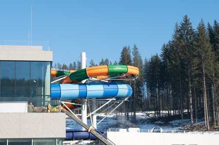 Brightly colored water slides rise above snowy ground, inviting thrill-seekers for a fun day in an amusement park surrounded by lush pine trees and a brilliant sky.の写真素材