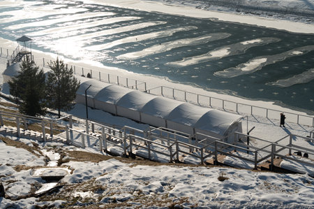 Frost blankets the ground while a frozen river reflects the sun's light. A charming shelter offers...