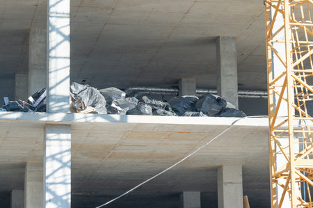 Workers clear debris from upper levels while construction continues on a building. Sunlight plays on concrete, creating a dynamic interplay of light and shadow throughout the site.の写真素材