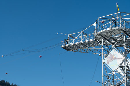 Beneath a clear blue sky, an adventurous group stands poised on a zipline platform, ready to launch into the thrill of soaring across the landscape.の写真素材