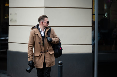 A well-dressed man walks confidently down the street, camera in hand, ready to capture the essence of city life during a cool, overcast day.の写真素材