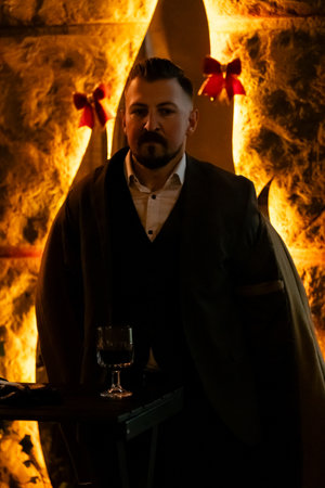 A well-dressed man stands confidently by a table, holding a drink in a warmly lit venue, embodying the spirit of an elegant evening with festive decor and intimate ambiance.の写真素材