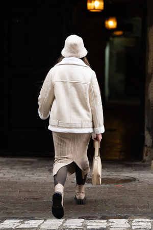 A woman dressed in a chic cream outfit strolls confidently through a narrow cobblestone street surrounded by soft glowing lights, embodying urban sophistication.の写真素材