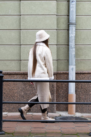 A young woman in a chic outfit walks gracefully along a city path, showcasing her sense of style against a backdrop of urban architecture.の写真素材