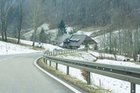 Curving along a peaceful road, the path leads to a charming cabin surrounded by serene snow-covered hills, creating a perfect winter escape in nature's embrace.の写真素材