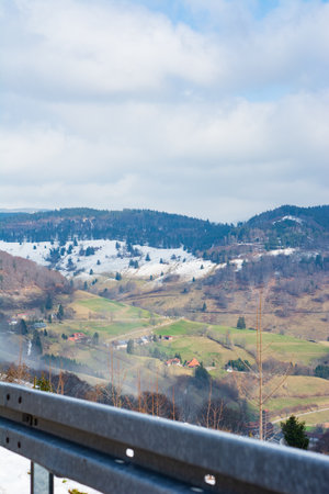 A stunning winter view unveils green valleys with charming homes, nestled among gentle hills and a cloudy sky, inviting tranquility and reflection.の写真素材