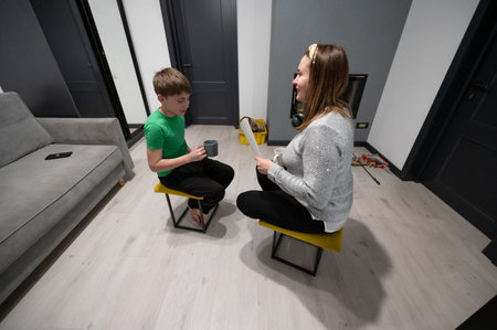 A cheerful mother engages in a heartfelt conversation with her son while seated on stylish stools in their bright living room, fostering a warm bond over coffee and moments shared.の写真素材