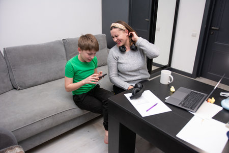 A mother and her son enjoy quality time together, sharing laughter while playing video games in their modern living room, evoking a sense of togetherness and joy.の写真素材