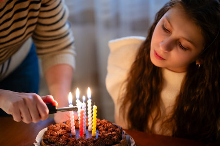 A young girl gazes with excitement as candles are lit on a beautifully decorated chocolate cake,...