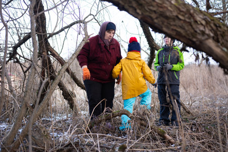 Family adventure in the winter woods captures a mother guiding her children through trees and...