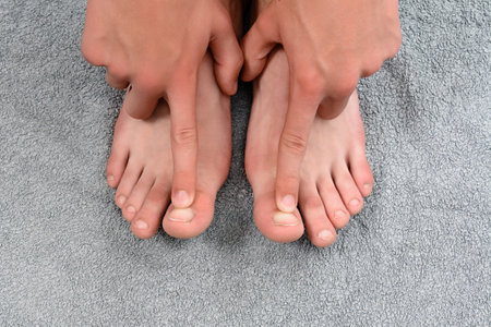 A person's hands carefully touch their feet, which are resting on a gray, textured towel. The image focuses on the detail of the feet and hands.の写真素材